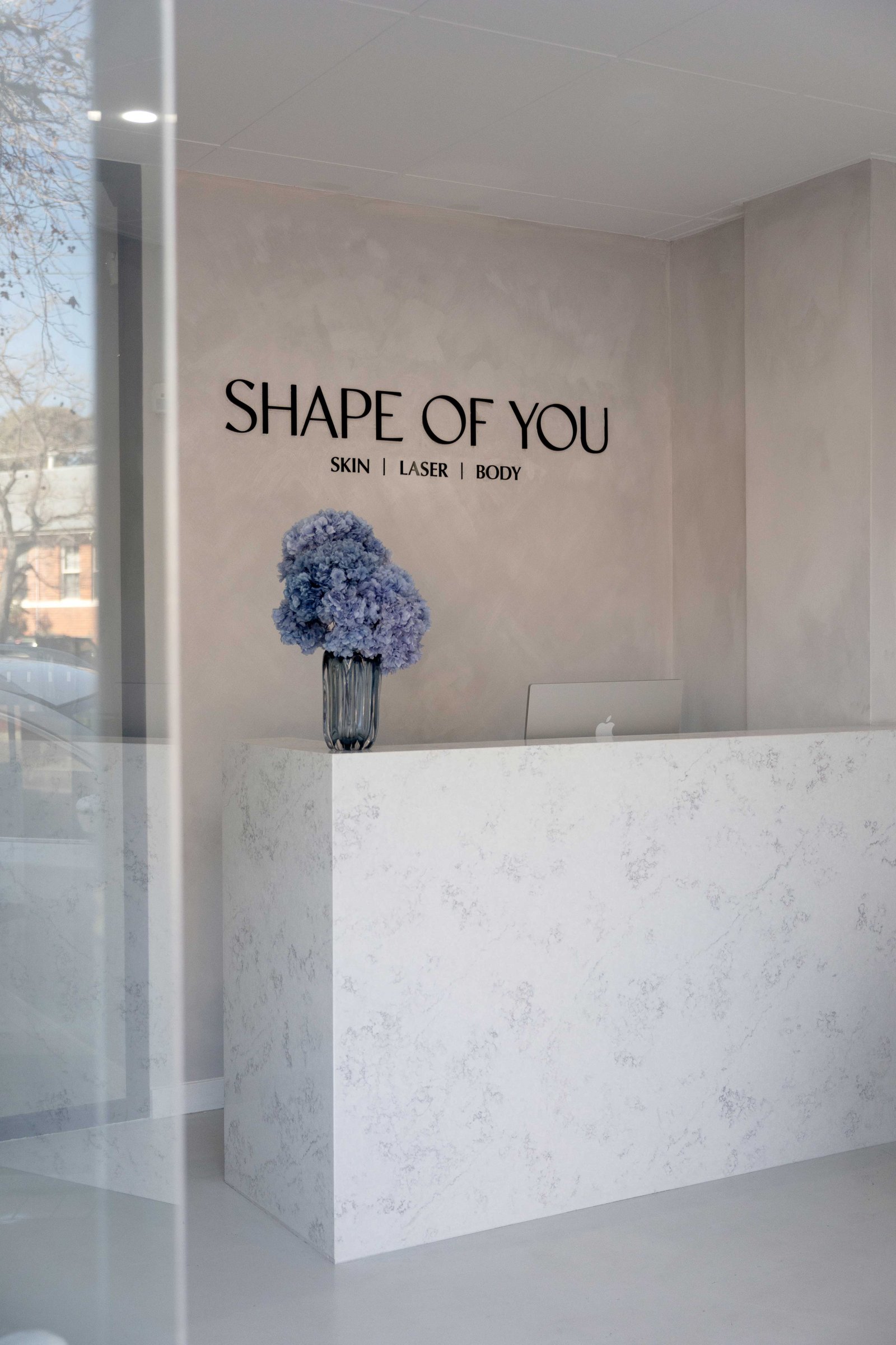 Shape of You Perth clinic reception desk with the Skin Laser Body signage and blue hydrangeas